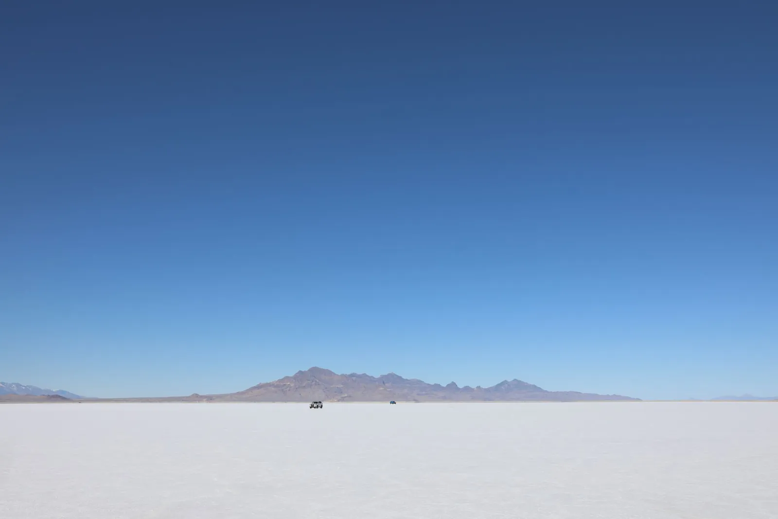 A salt flat under a deep blue sky, with low mountains on a straight horizon